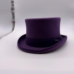 May include: A purple top hat with a dark purple band. The hat has a tall, cylindrical crown and a wide brim. The hat is made of a felt-like material and is suitable for formal events or costume parties.