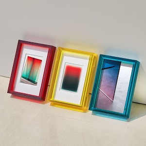 Peut inclure: Trois cadres aux couleurs vives, rouge, jaune et bleu. Chaque cadre contient une œuvre d'art abstraite unique avec un passe-partout blanc. Les cadres sont posés contre un mur blanc.