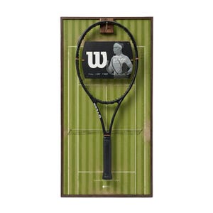 Puede incluir: Una raqueta de tenis Wilson Pro Staff negra exhibida sobre un fondo verde enmarcado que se asemeja a una cancha de tenis. La raqueta está montada con una imagen en blanco y negro de un jugador de tenis. El logotipo de Wilson es visible.