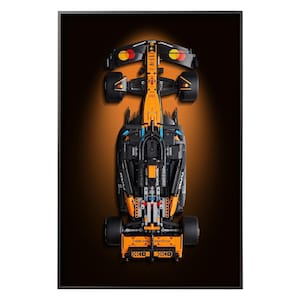 Peut inclure: Vue de dessus d'une maquette de voiture de course noire et orange. Le modèle présente un design détaillé avec des composants visibles, notamment des roues, un cockpit et des logos de sponsors. La voiture est sur un fond orange et noir dégradé.