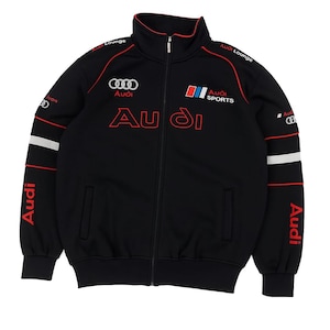 May include: Black zip-up track jacket with red and white accents. The jacket features the Audi logo and text in red, with "Audi Sports" printed on the chest. White stripes are on the sleeves, and "Audi" is printed vertically on the sleeves.