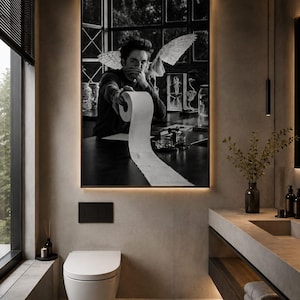 May include: A rectangular wall art print featuring a black and white photograph of a person with wings holding a roll of toilet paper, displayed in a modern bathroom with a white wall-mounted toilet and a concrete vanity with stacked towels.