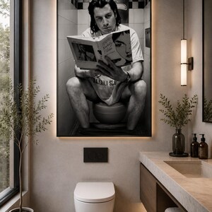 May include: A large rectangular wall art print featuring a black and white photograph of a person sitting on a toilet reading a book titled Modesty Blaise, with the text Banana Slug visible on their shirt, displayed in a modern bathroom setting.