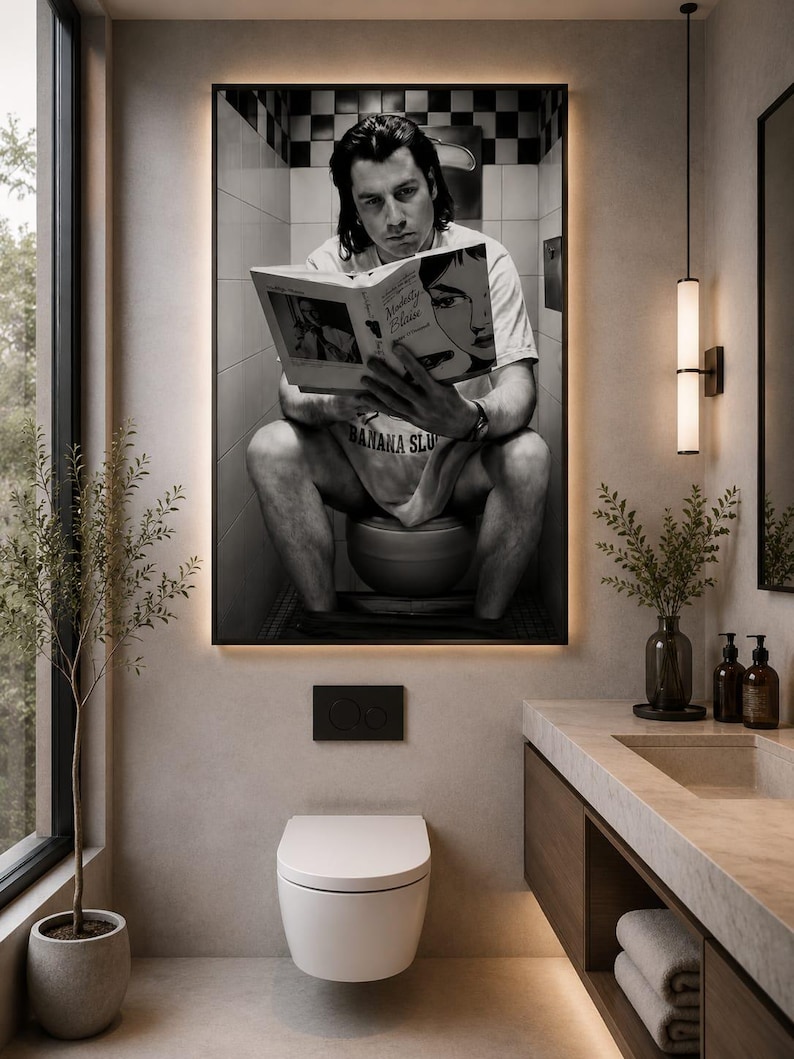 May include: A large rectangular wall art print featuring a black and white photograph of a person sitting on a toilet reading a book titled Modesty Blaise, with the text Banana Slug visible on their shirt, displayed in a modern bathroom setting.