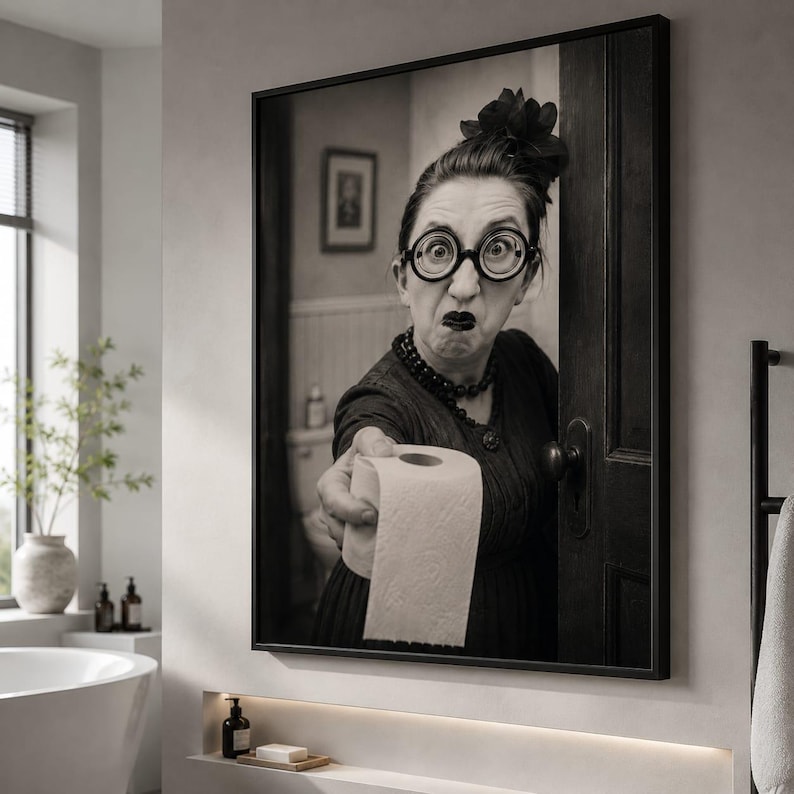 May include: A black and white framed wall art print depicting a person with dark hair in an updo, wearing round glasses and a dark dress, holding out a roll of toilet paper. The person has a surprised expression with wide eyes and dark lips.