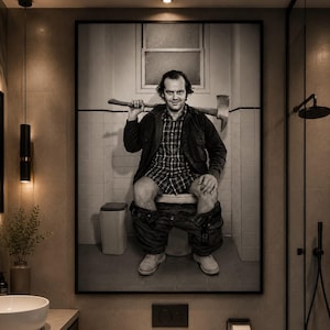 May include: A framed black and white wall art print depicting a person with dark hair wearing a plaid shirt and jacket, sitting on a toilet with trousers around their ankles, holding an axe across their shoulders in a tiled bathroom setting.