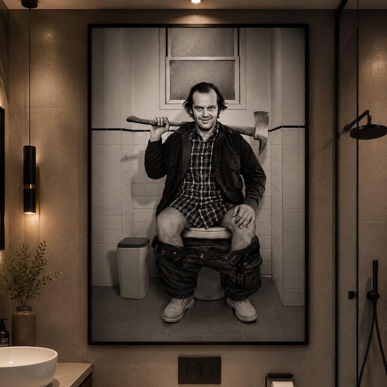 May include: A framed black and white wall art print depicting a person with dark hair wearing a plaid shirt and jacket, sitting on a toilet with trousers around their ankles, holding an axe across their shoulders in a tiled bathroom setting.