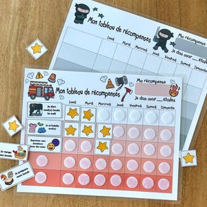 May include: Two laminated reward charts with white backgrounds and grids for days of the week. One features ninja illustrations and the other a fire truck, traffic cone, and axe. Both include text in French, yellow star stickers, and velcro dots.