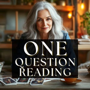 Op de afbeelding: Een vrouw met grijs haar glimlacht en houdt een bord vast met de tekst "ONE QUESTION READING". Tarotkaarten en een kopje thee liggen op de houten tafel. De achtergrond omvat planten en een warme, uitnodigende interieursetting.