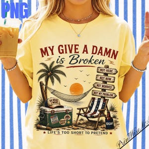 May include: A pale yellow t-shirt featuring a graphic print of a beach scene with a palm tree, a hammock, a cooler, and a beach chair. The text reads: MY GIVE A DAMN is Broken, NOT HERE, NOT NOW, NOT WORRIED, NOT MY PROBLEM, and IDGAF on a bottle.
