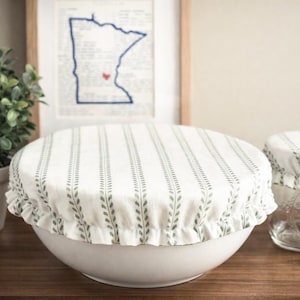 May include: Two fabric bowl covers with an elasticized ruffled edge, featuring a white background with a repeating vertical pattern of small green leaves. One cover is fitted over a large white bowl, and the smaller cover is on a glass jar.