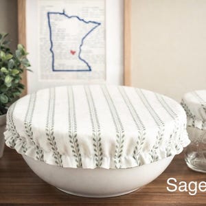 May include: White bowl and jar covers with a sage leaf pattern. The covers have a ruffled edge and are designed to fit over bowls and jars. The text "Sage Leaf" is visible in the image. The covers are made of fabric.