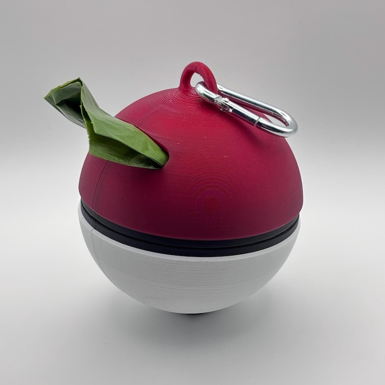 May include: A red and white sphere-shaped pet waste bag dispenser with a silver carabiner clip. A green bag is partially pulled out of the top. The dispenser is designed to hold and dispense waste bags for pets.