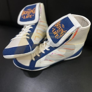 Puede incluir: Par de zapatillas de boxeo blancas y azules con el texto "NO BOXING NO LIFE" en la lengüeta. Las zapatillas tienen un diseño de caña alta con cordones blancos y una parte superior de malla. Zapatillas de boxeo.