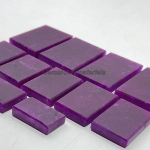 May include: A collection of rectangular, polished purple gemstones. The gemstones are arranged in a grid pattern, with a slight variation in color and texture. The image includes the text "GemsRAWmaterials".