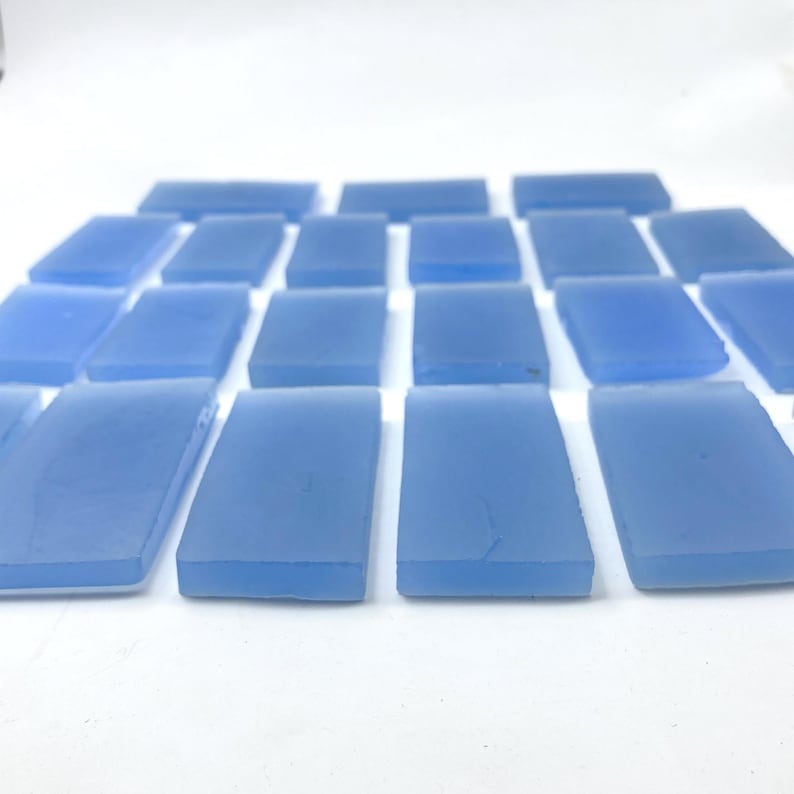 May include: A collection of rectangular, light blue glass tiles. The tiles are arranged in a grid pattern, with a frosted appearance. The colour is a soft, muted blue, and the edges appear slightly rounded. The tiles are likely for mosaic or decorative use.