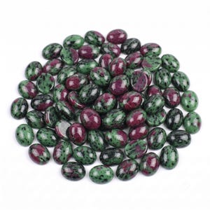 Op de afbeelding: Een verzameling van talrijke ovaalvormige cabochons met een gevlekt patroon van diep magenta en donker bosgroen. Elke steen heeft een glad, gepolijst oppervlak met een glanzende afwerking, wat een natuurlijke mix van kleuren in de groep laat zien.