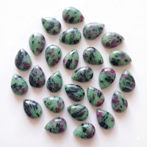 Peut inclure: Une collection de vingt-quatre cabochons en forme de goutte d'eau composés de zoïsite avec des cristaux de rubis incrustés. Chaque pierre présente une surface lisse et polie avec un motif tacheté de vert clair, de noir et de rouge magenta.