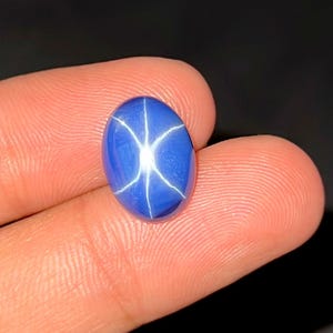 Peut inclure: Une pierre précieuse saphir étoilé bleu de forme ovale présentant un motif d'étoile à six branches distinct sur sa surface lisse et polie. La pierre affiche une couleur bleue profonde et vibrante avec un reflet blanc brillant.
