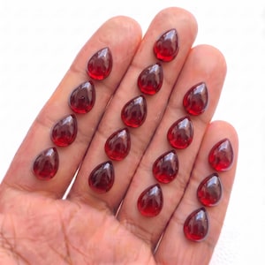 May include: A collection of fourteen loose, deep red, pear-shaped gemstones with a smooth, polished surface. Each stone features a faceted top and a rounded base, displaying a consistent translucent crimson color throughout the entire set.