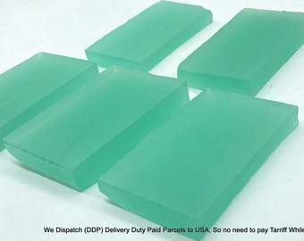 May include: Six rectangular, translucent, teal-colored soap bars arranged on a white surface. The bars have a smooth, slightly rounded top edge and a flat bottom. The soap appears to be handmade.