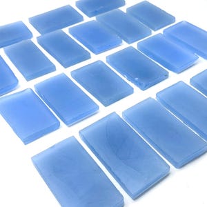 May include: A collection of rectangular, light blue glass tiles arranged on a white surface. The tiles have a frosted appearance and are evenly spaced, creating a pattern. The tiles are approximately 2.5 cm by 5 cm.