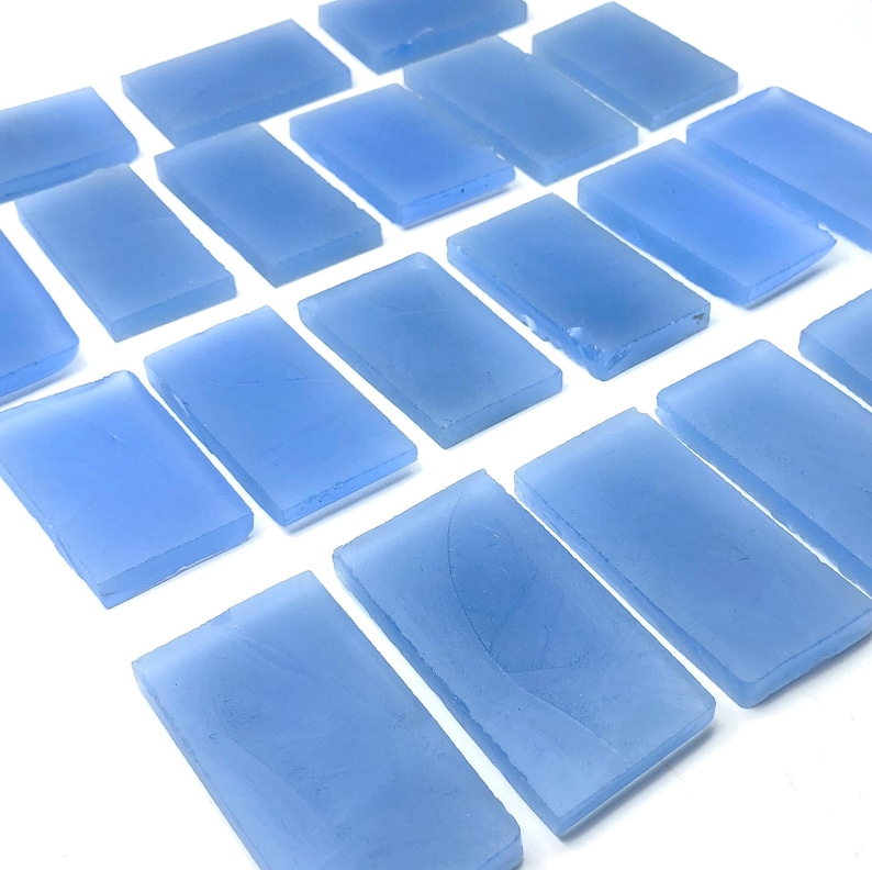May include: A collection of rectangular, light blue glass tiles arranged on a white surface. The tiles have a frosted appearance and are evenly spaced, creating a pattern. The tiles are approximately 2.5 cm by 5 cm.