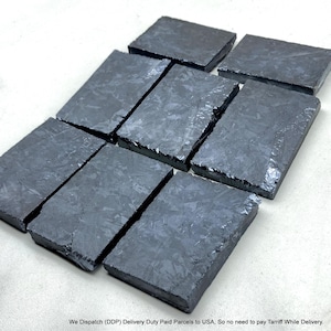 May include: A collection of eight rectangular blocks with a dark, charcoal-grey finish and a distinct, crystalline, marbled texture across their surfaces. Each block features sharp, clean edges and a reflective, glossy sheen that highlights the intricate, layered pattern within the material.