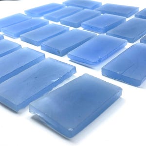 May include: A group of rectangular, translucent, light blue glass tiles. The tiles are arranged in rows and appear handmade. The edges are slightly rounded, and the surface has a subtle texture. The overall effect is of a cool, aquatic aesthetic.