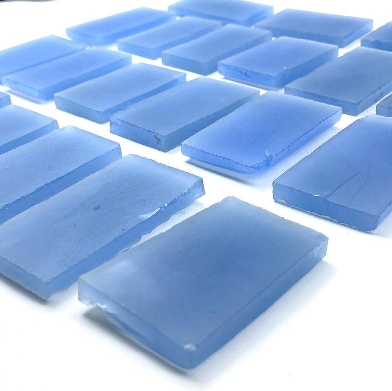 May include: A group of rectangular, translucent, light blue glass tiles. The tiles are arranged in rows and appear handmade. The edges are slightly rounded, and the surface has a subtle texture. The overall effect is of a cool, aquatic aesthetic.
