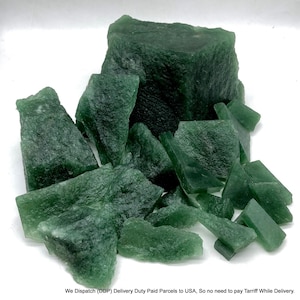 May include: A collection of raw, dark green mineral chunks with irregular, jagged edges and varying sizes. The stones exhibit a semi-translucent quality with a rough, crystalline texture, clustered together to form a dense, uneven pile of natural rock.