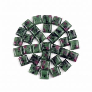 Peut inclure: Une collection de pierres précieuses rubis sur zoïsite taillées en carré disposées en cercle. Chaque pierre présente une base verte tachetée avec des inclusions noires de hornblende et des taches rose magenta vif sur la surface.