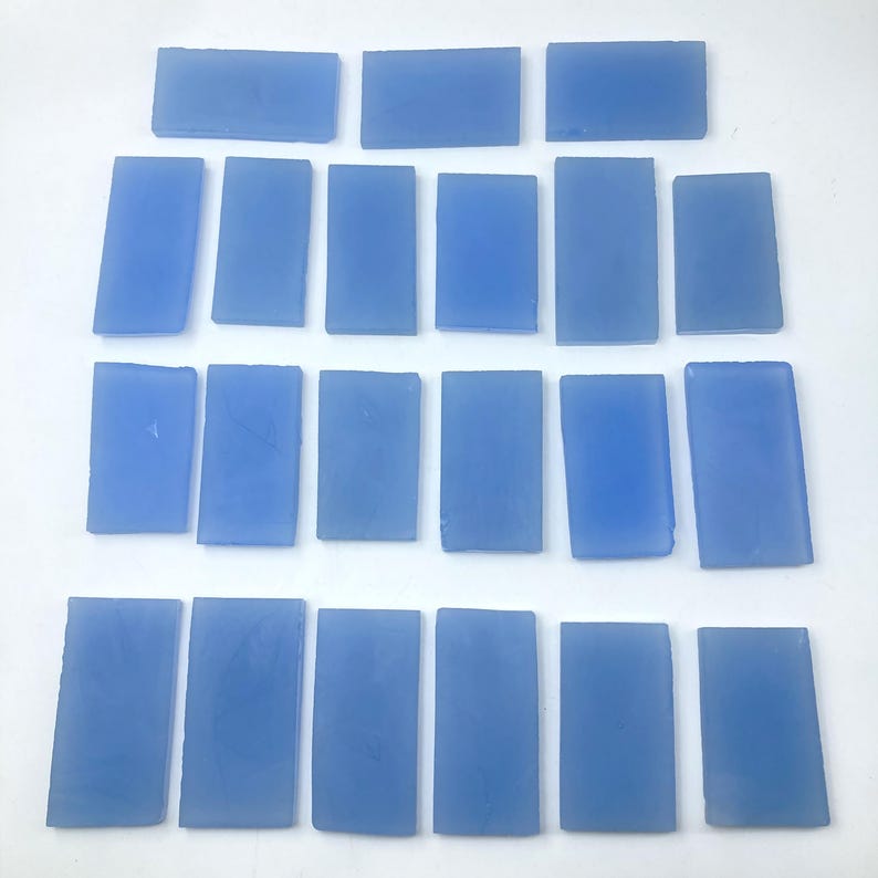 May include: A collection of twenty-one rectangular, light blue glass tiles. The tiles are arranged in a grid pattern, with varying sizes and shapes. The glass has a smooth, translucent appearance, and the colour is consistent throughout.