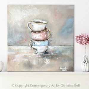 Puede incluir: Una pintura de tres tazas de té apiladas con ribetes dorados. Las tazas son blancas, rosadas y azules. El fondo es gris claro con toques de rosa y azul. La firma del artista, "Christine Bell", está en la esquina inferior derecha.