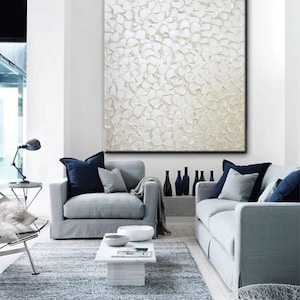 May include: A white textured abstract painting hangs on a white wall above two gray sofas with blue throw pillows. The sofas are in a living room with a gray rug and a white coffee table.
