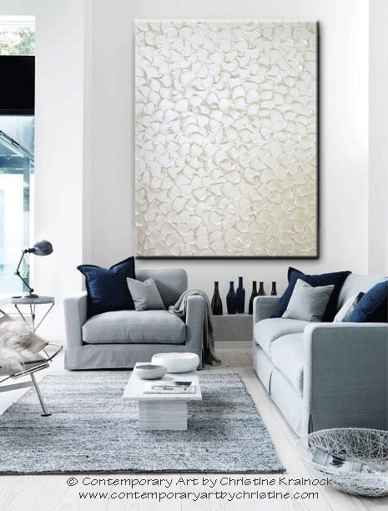 May include: A white textured abstract painting hangs on a white wall above two gray sofas with blue throw pillows. The sofas are in a living room with a gray rug and a white coffee table.
