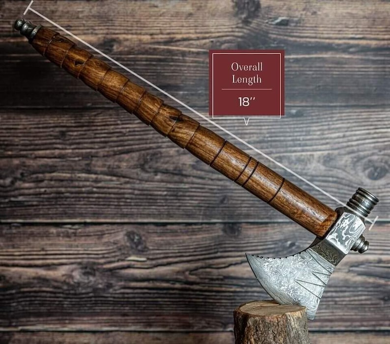 May include: A handcrafted tomahawk with a wooden handle and a metal head. The overall length is 45.7 cm. The handle is a dark brown color with a textured design. The metal head has an etched pattern and a silver finish.