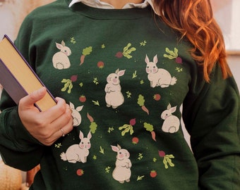 May include: A dark green sweatshirt with a white rabbit and vegetable pattern. The sweatshirt has a crew neck and long sleeves.