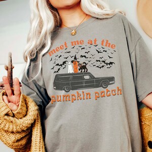 May include: A gray t-shirt with a graphic of a hearse with a ghost, witch, and black cat on top. The text "Meet me at the pumpkin patch" is printed on the shirt.