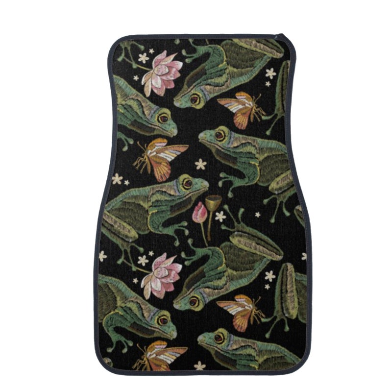 Puede incluir: Alfombrilla para coche negra con un patr&oacute;n repetido de ranas verdes, flores rosas y mariposas.