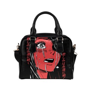 May include: Black handbag featuring a red and white illustration of a crying face. The image has Japanese text on the side. The bag has a top handle and a detachable shoulder strap. The bag is made of a smooth material.