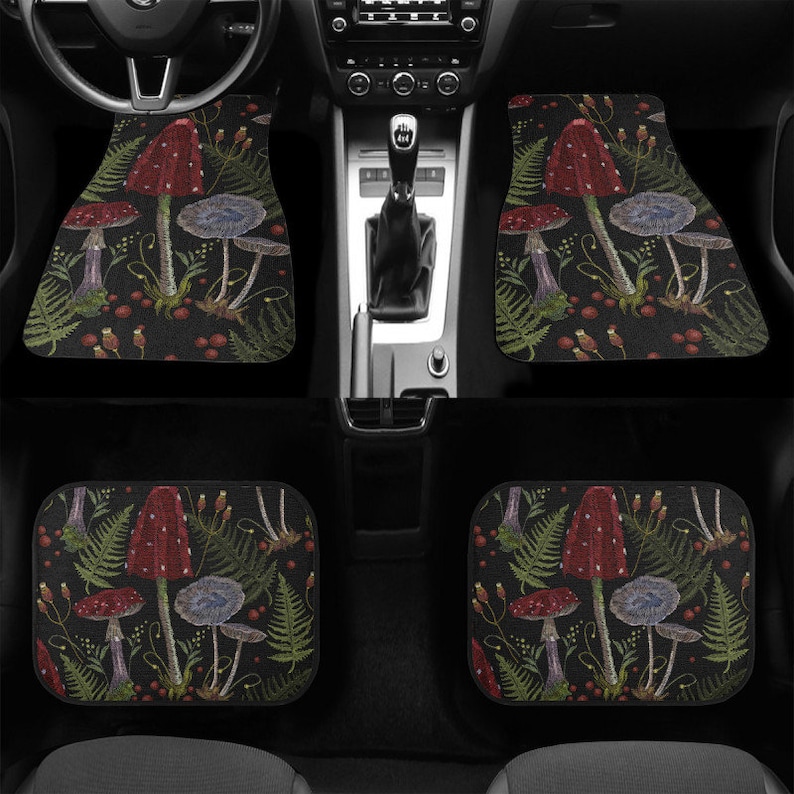May include: Set of four black car floor mats featuring a mushroom and fern design. The mats have a dark background with red and white mushrooms, green ferns, and small red berries.