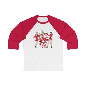 May include: A white and red baseball tee shirt with a Christmas-themed design featuring two women in red dresses standing next to a large candy cane.