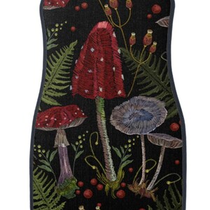 May include: A black car floor mat with an embroidered design of red and white mushrooms, blue mushrooms, green ferns, and red berries.