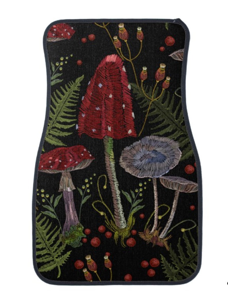 May include: A black car floor mat with an embroidered design of red and white mushrooms, blue mushrooms, green ferns, and red berries.