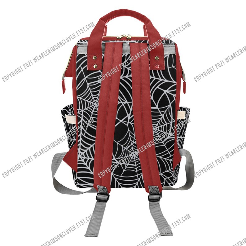May include: A black and white spiderweb-patterned backpack with red detailing. The backpack has red shoulder straps, a top handle, and side pockets. It features a zip closure and grey adjustable straps. The text "COPYRIGHT 2021 WEARECRIMSONCLOVER.ETST.COM" is visible.