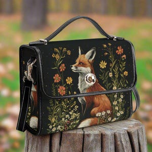 May include: A black leather satchel handbag with a fox and floral design. The bag has a long strap and a top flap closure.