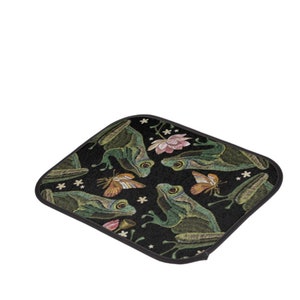Puede incluir: Un posavasos de tela negro con un patr&oacute;n repetido de ranas verdes, mariposas y flores rosas. El dise&ntilde;o est&aacute; bordado en la tela.