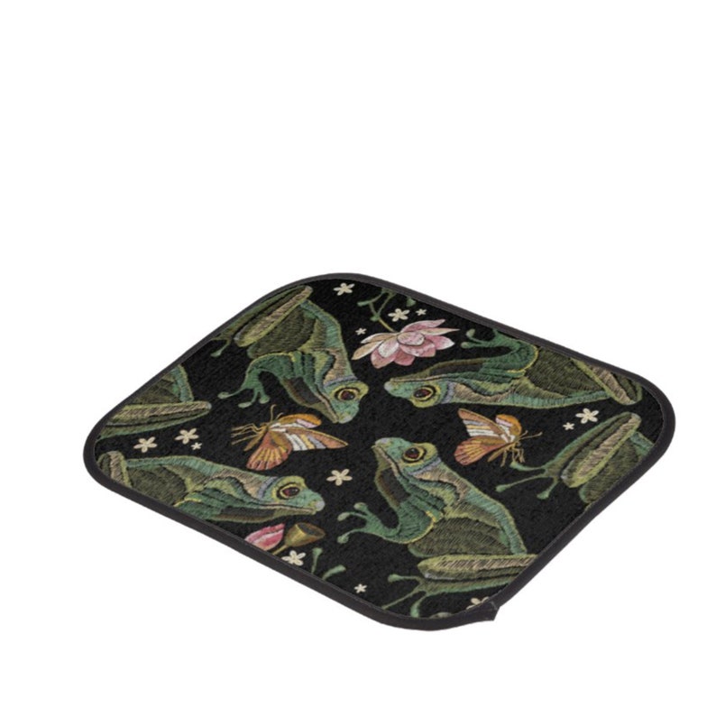 Puede incluir: Un posavasos de tela negro con un patr&oacute;n repetido de ranas verdes, mariposas y flores rosas. El dise&ntilde;o est&aacute; bordado en la tela.