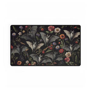 May include: A rectangular mousepad featuring a repeating pattern of bats and flowers on a black background. The bats are depicted in shades of gray with their wings spread, interspersed with colorful flowers in red, orange, yellow, and blue.